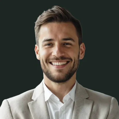 Smiling young man with short hair and beard wearing a light-colored blazer and white shirt against a dark background.